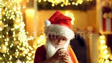 圣诞老人的孩子拿着圣诞饼干和牛奶在圣诞树的背景下。 圣诞饼干和牛奶
